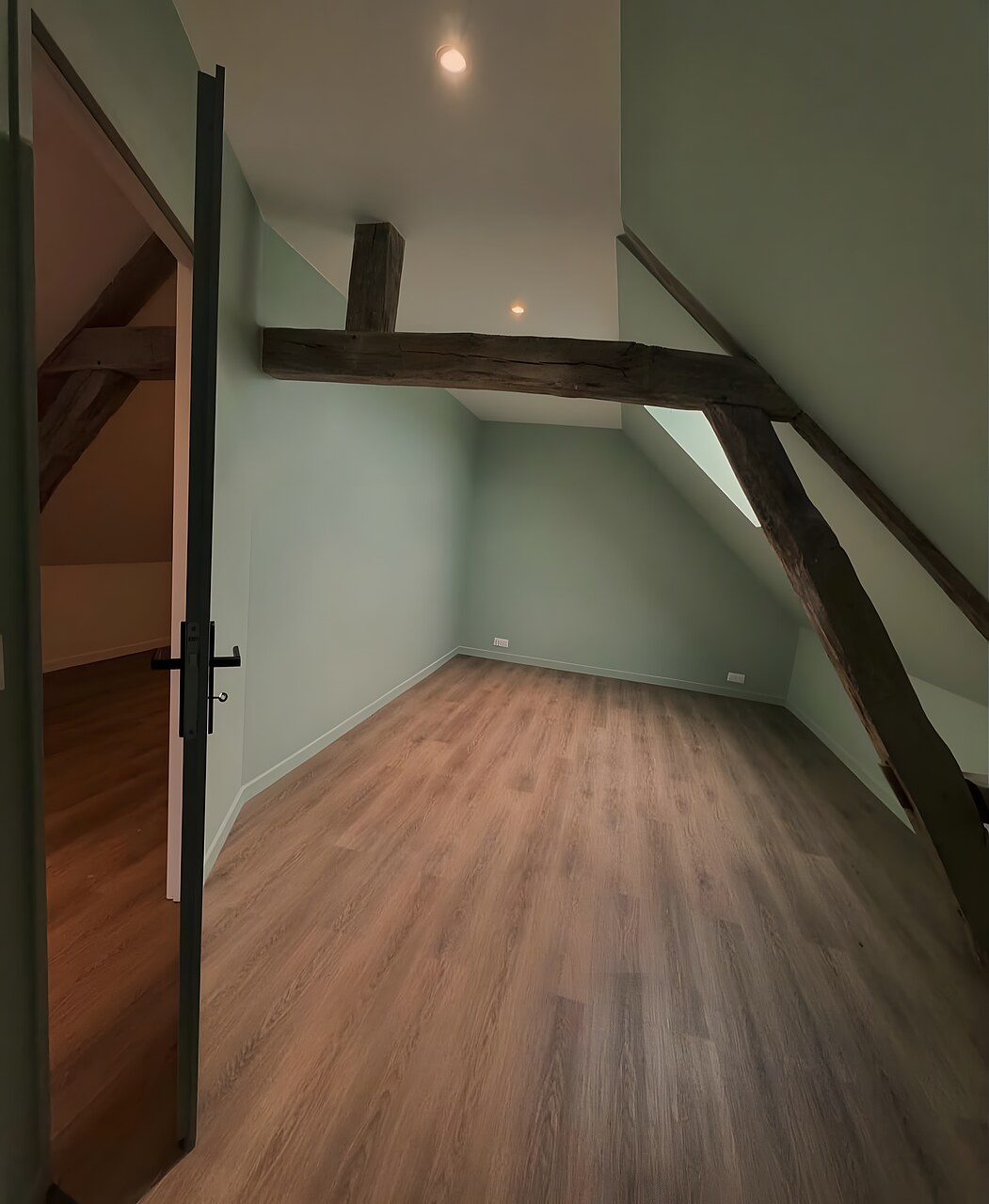Combles après aménagement : pièce habitable avec parquet, peinture vert sauge et poutres apparentes