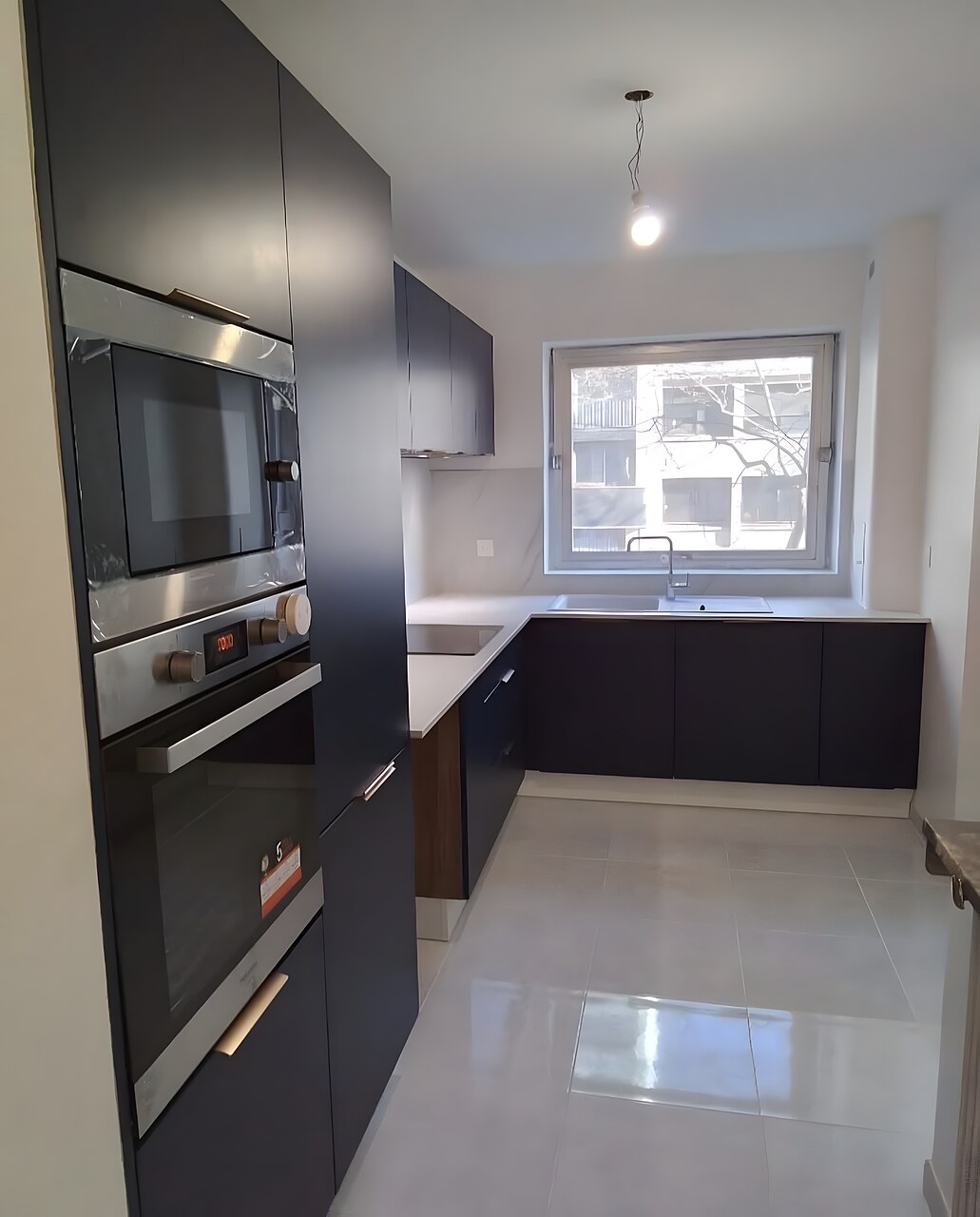 Cuisine après rénovation : meubles bleu nuit, plan de travail clair, carrelage gris perle